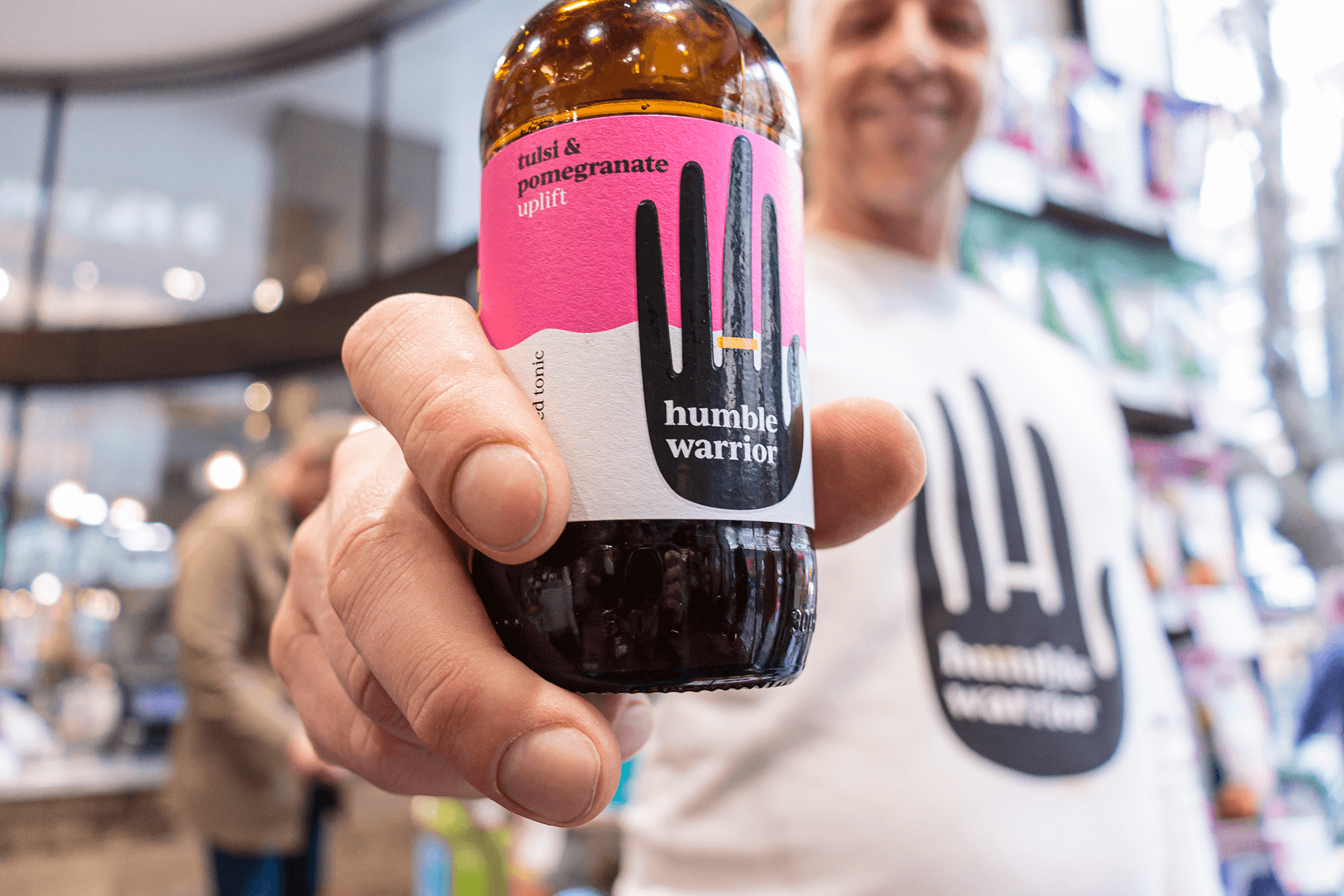 Man holding a ‘Humble Warrior’ adaptogenic soft drink. The drink is in focus at the forefront of the photo and the man is out of focus behind it.