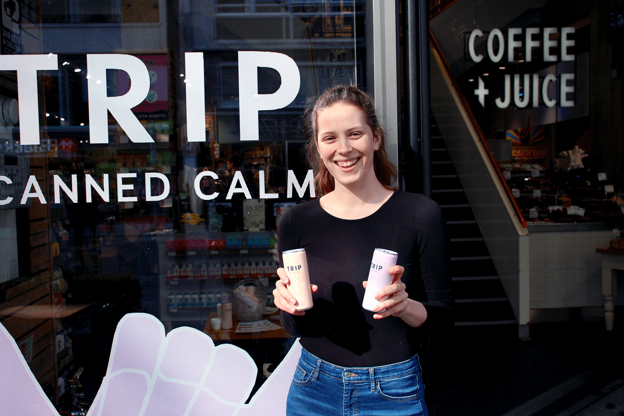 Young, smiley female brand ambassador standing outside Planet Organic on Tottenham Court Road holding a Trip CBD drinks can. 